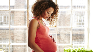 A young, 20-something African American mother-to-be with her hand resting on her pregnant belly