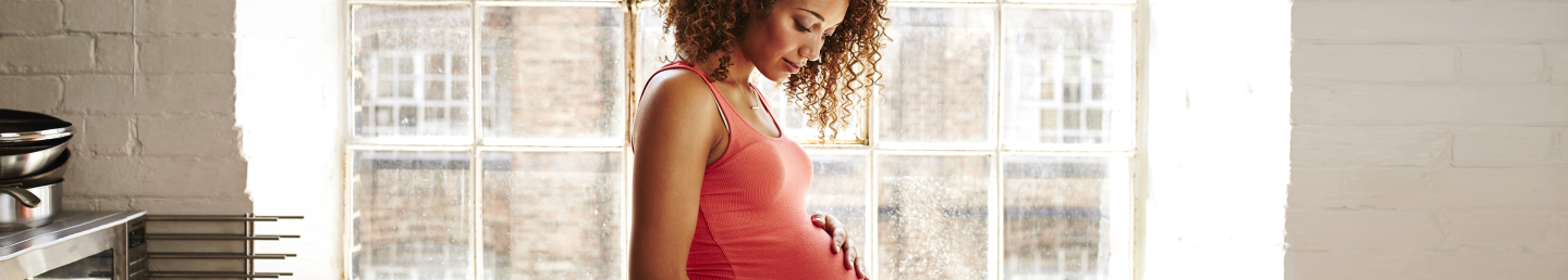 A young, 20-something African American mother-to-be with her hand resting on her pregnant belly